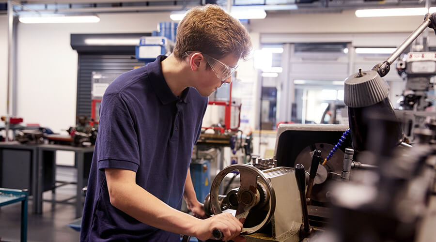 Ausbildung mit ASS, Foto: Monkey Business Images/Shutterstock Ein junger Azubi steht an einer Drehbank, er trägt eine Schutzbrille.